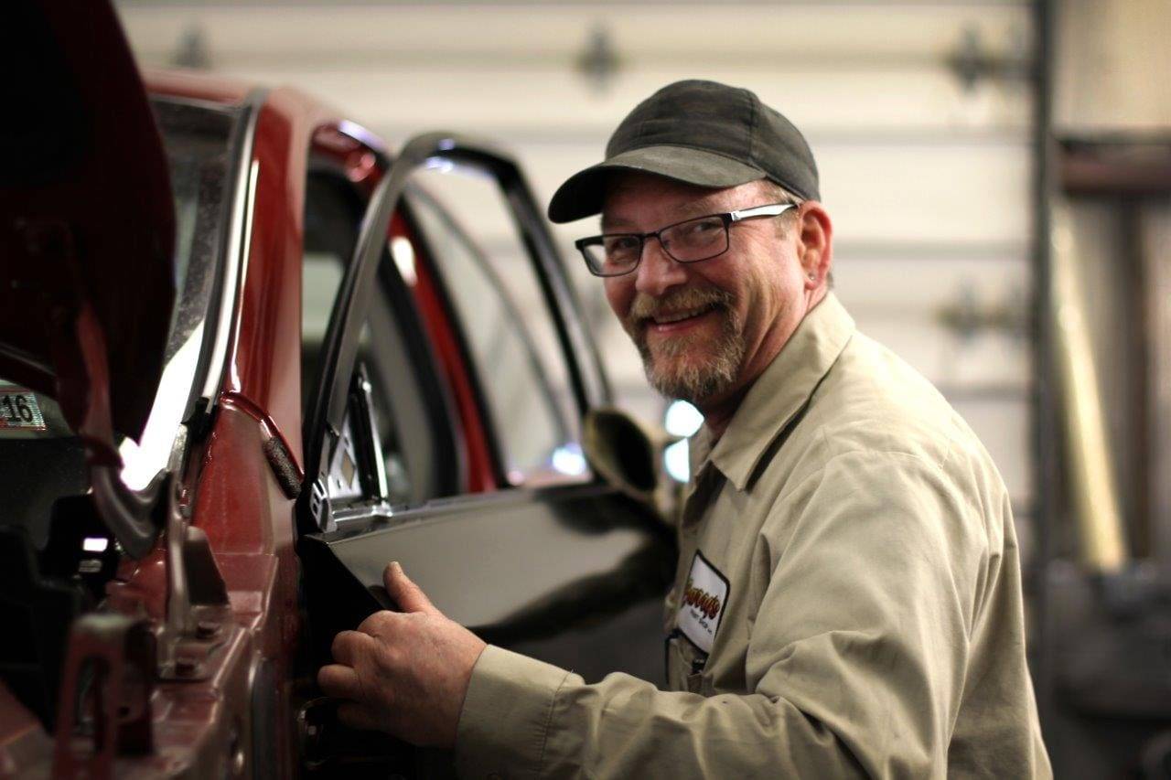 Smiling auto body technician working on vehicle repair at Barry's Paint Shop, showcasing expertise in collision repair services.