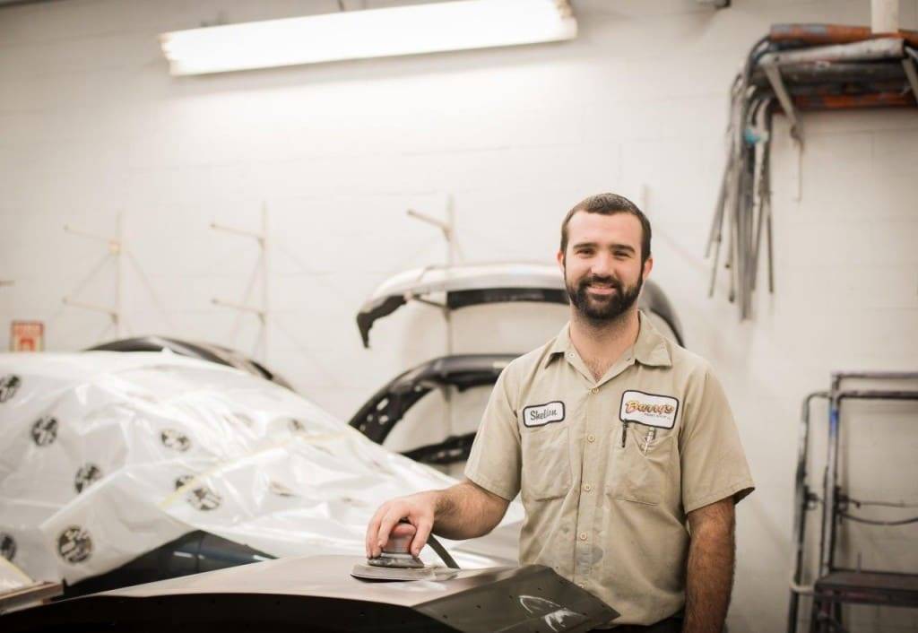 Auto body technician smiling in a repair shop, showcasing quality workmanship and dedication to collision repairs and refinishing at Barry's Paint Shop.