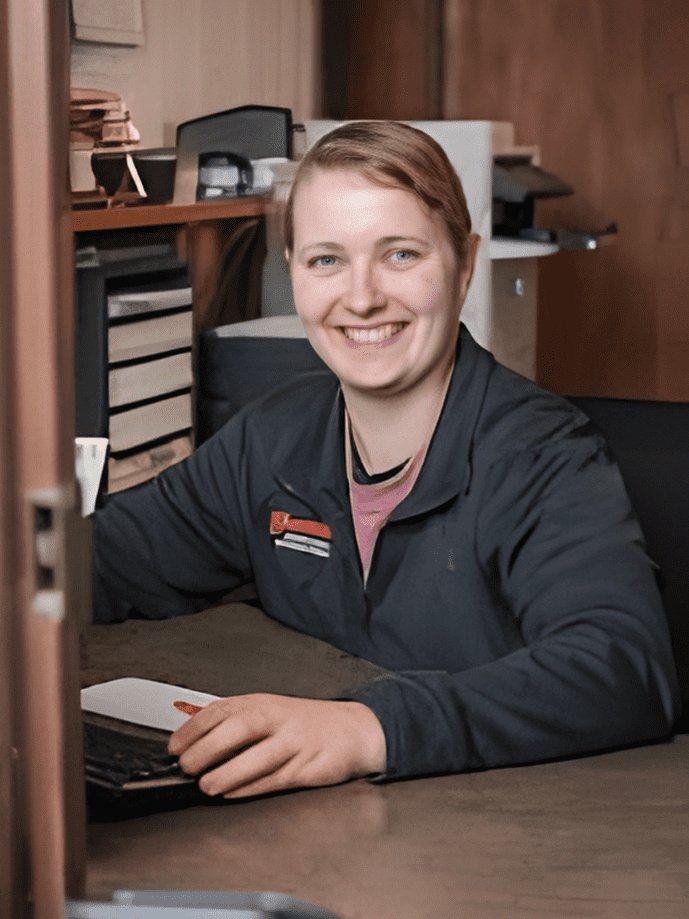 Kimberly Sensenig, bookkeeper at Barry's Paint Shop, smiling while working at her desk with paperwork and a laptop, emphasizing the team's commitment to customer service and satisfaction.