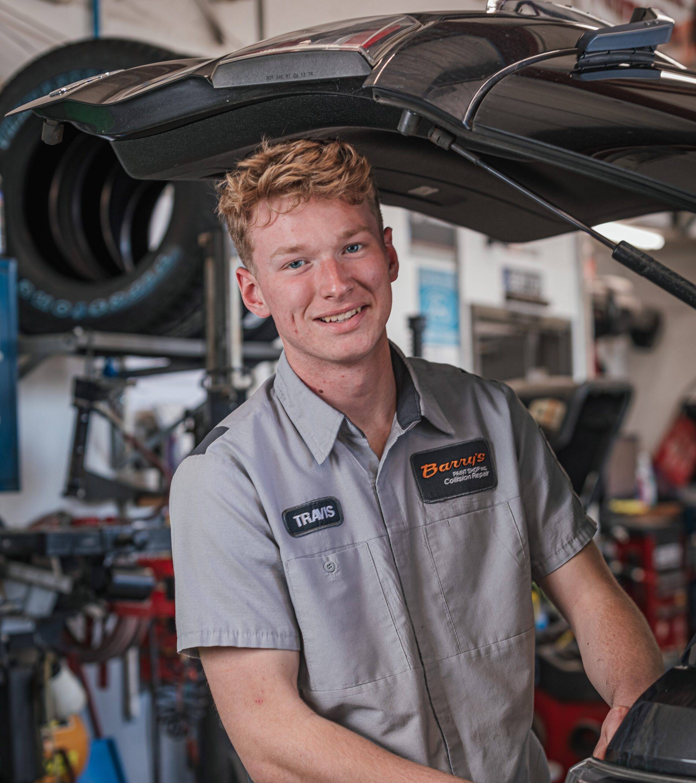 Travis Horning, employee at Barry's Paint Shop, smiling while working on a vehicle in the repair shop environment, showcasing commitment to quality automotive services.